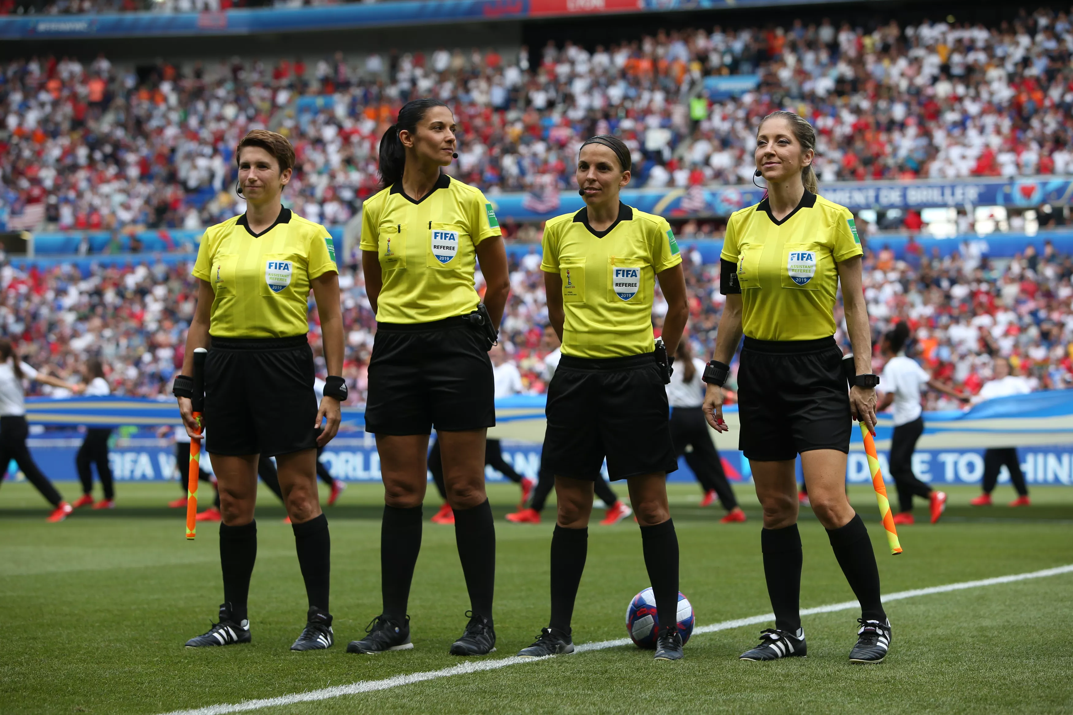 Four female FIFA referees in yellow uniforms on football pitch